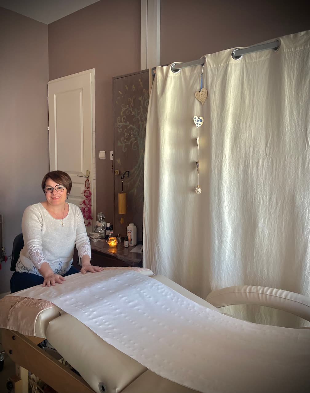 Laetitia Dionnau - Réflexologue à Puisserguier - portrait assis devant table de réflexo comfortable Laetitia Dionnau - Réflexologue à Puisserguier assise à sa table de massage dans son cabinet de rélfexologie